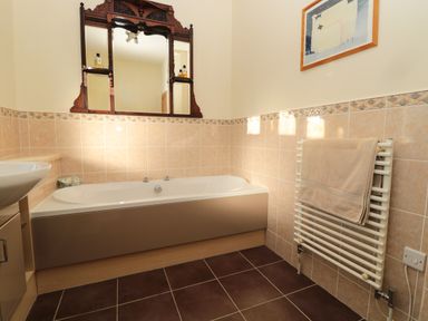 A bathroom with a bathtub a wooden framed mirror a towel radiator with a towel and a framed picture on the wall at Whinstones at 4 The Villas in Embleton