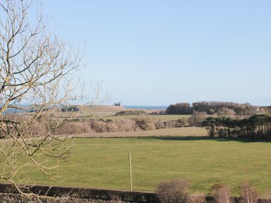 A landscape with green fields trees and distant ruins near the coast at Whinstones at 4 The Villas in Embleton