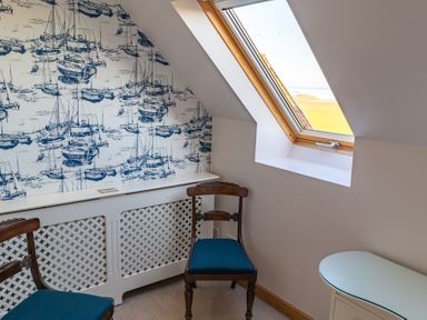 A small corner with two wooden chairs with blue seats a skylight window and a radiator cover with boat wallpaper at Whinstones at 4 The Villas in Embleton