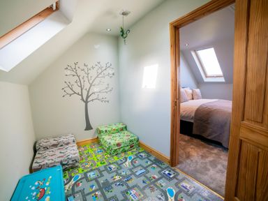 A small playroom with a tree wall decal toy storage and a colorful play mat connected to a bedroom with a bed and skylight windows at Whinstones at 4 The Villas in Embleton
