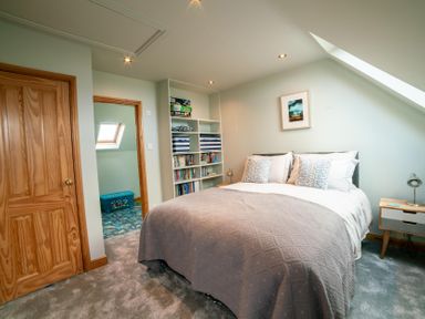 A bedroom with a double bed bedside tables a bookshelf and a wooden door at Whinstones at 4 The Villas in Embleton
