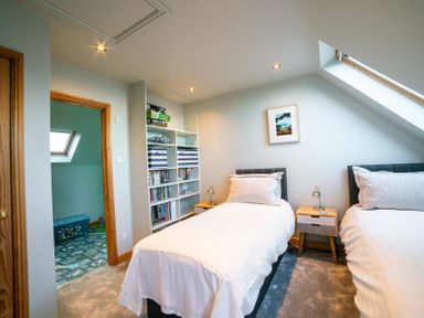 A bedroom with two single beds a small wooden bedside table shelves with books and games and a skylight window at Whinstones at 4 The Villas in Embleton