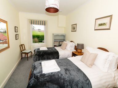 A bedroom with two single beds towels on beds a chair window and nightstand at Whinstones at 4 The Villas in Embleton