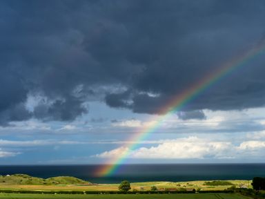 A rainbow over grassy fields and ocean with dark clouds in the sky at Whinstones at 4 The Villas in Embleton