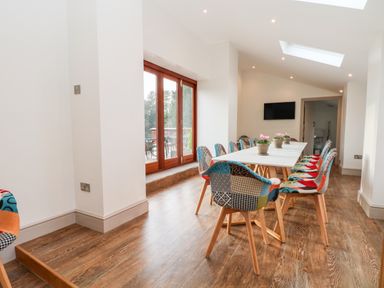 A dining room with a long white table surrounded by colorful chairs and potted plants on the table at Lakeside Village Lodges & The Potting Shed in Capesthorne near Macclesfield