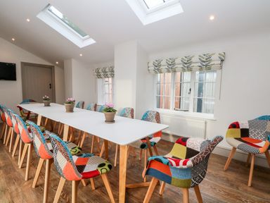A dining room with a long white table and colorful patchwork chairs with flowers on the table at Lakeside Village Lodges & The Potting Shed Capesthorne near Macclesfield