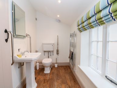 A bathroom with a pedestal sink, toilet, mirror, towel rack, and window with striped blinds at Lakeside Village Lodges & The Potting Shed in Capesthorne near Macclesfield