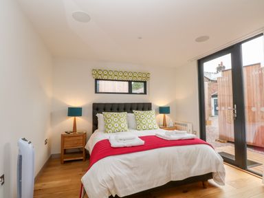 A bedroom with a double bed two bedside tables with lamps and glass doors leading outside at Lakeside Village Lodges & The Potting Shed in Capesthorne near Macclesfield