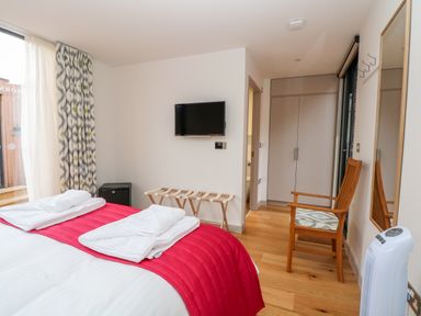 A bedroom with a bed with white and red bedding a wooden chair a wall-mounted television a luggage rack and a wardrobe at Lakeside Village Lodges & The Potting Shed in Capesthorne near Macclesfield