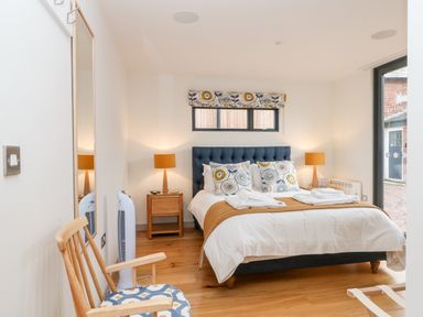 A bedroom with a bed linens bedside tables lamps a wooden chair and a mirror at Lakeside Village Lodges & The Potting Shed in Capesthorne near Macclesfield