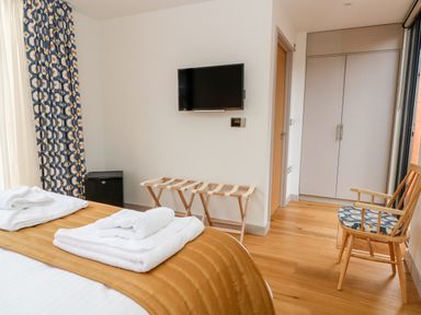 A bedroom with a bed with folded towels a TV mounted on the wall a wooden chair with a patterned cushion and a wardrobe at Lakeside Village Lodges & The Potting Shed in Capesthorne near Macclesfield