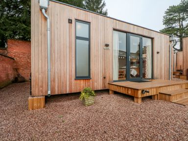 A wooden cabin exterior with a small deck and potted plant at Lakeside Village Lodges & The Potting Shed Capesthorne near Macclesfield
