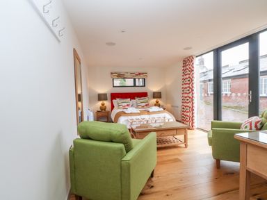 A bedroom with two green armchairs a wooden coffee table and a bed with a red headboard at Lakeside Village Lodges & The Potting Shed Capesthorne near Macclesfield
