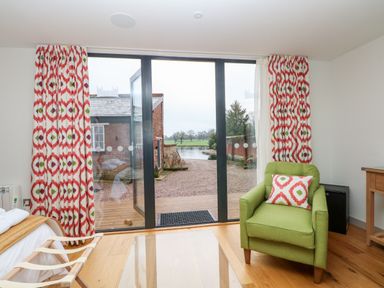 A room with a green armchair with a patterned cushion near glass doors with patterned curtains at Lakeside Village Lodges & The Potting Shed in Capesthorne near Macclesfield