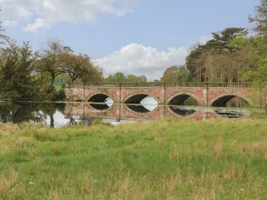 A stone arch bridge over a river with trees and grass at Lakeside Village Lodges & The Potting Shed in Capesthorne near Macclesfield