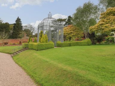 An outdoor garden area with a metal gazebo surrounded by trimmed hedges and trees at Lakeside Village Lodges & The Potting Shed Capesthorne near Macclesfield