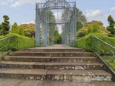 Stone steps leading to a metal garden archway surrounded by trimmed hedges and trees at Lakeside Village Lodges & The Potting Shed in Capesthorne near Macclesfield