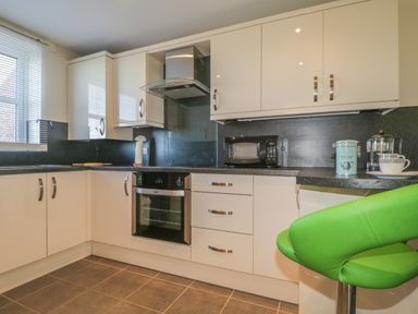 A kitchen with white cabinets a built-in oven a microwave coffee accessories and a green bar stool at Rowan Cottage in St Bees