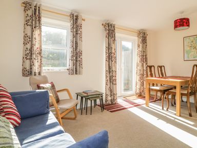 A living room with blue sofa beige chair wooden dining table with four chairs and floral curtains at Rowan Cottage in St Bees