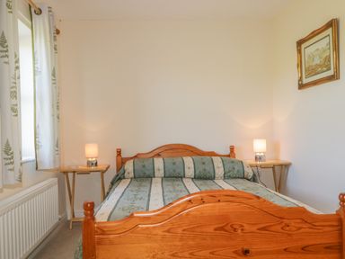 A bedroom with a wooden bed and two bedside tables with lamps at Rowan Cottage in St Bees