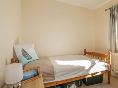 A bedroom with a wooden single bed a pillow with a sailboat design a bedside table with a lamp and framed picture at Rowan Cottage in St Bees