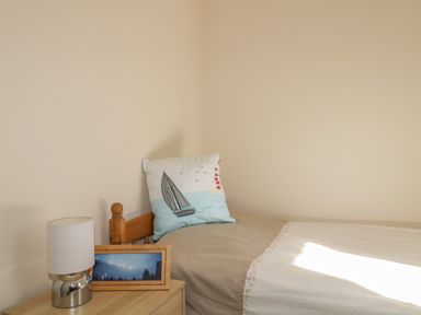 A single bed with a pillow with a sailboat and lighthouse design next to a bedside table with a lamp and framed photo at Rowan Cottage in St Bees