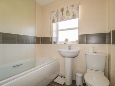 A bathroom with a bathtub a sink a toilet and a window with a patterned blind at Rowan Cottage in St Bees