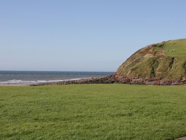 A coastal landscape with a grassy field a rocky hill and the ocean at Rowan Cottage in St Bees
