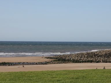 A view of a beach with people walking on the sand and rocks with the ocean in the background