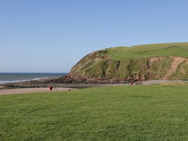 A coastal landscape with green grassy fields a sandy beach rocky cliffs and the sea at Rowan Cottage in St Bees