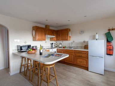 A kitchen with wooden cabinets a countertop with stools a microwave a refrigerator and kitchen utensils at Willow Barn in Cucklington near Wincanton