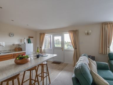 A kitchen and living area with a countertop and stools and a sofa near a door with curtains at Willow Barn in Cucklington near Wincanton