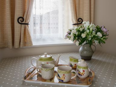 A table with a polka dot tablecloth a tray with tea set and a vase with flowers by a window with curtains at Willow Barn in Cucklington near Wincanton