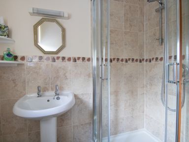 A bathroom with a white pedestal sink and dual taps next to a glass door shower enclosure with tiled walls at Willow Barn in Cucklington near Wincanton