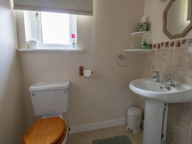 A bathroom with a toilet with wooden seat a sink with two taps a small window with toiletries and shelves with soap and tissues at Willow Barn in Cucklington near Wincanton