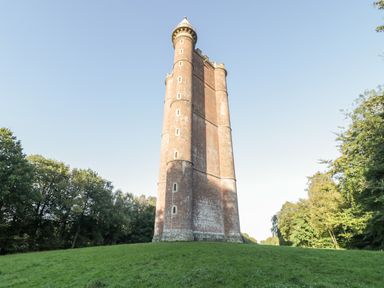 A tall brick tower with small windows surrounded by grass and trees at Willow Barn in Cucklington near Wincanton