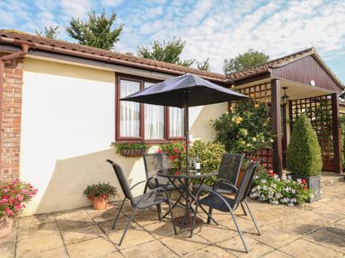 An outdoor patio with a round table and four chairs under an umbrella at Willow Barn in Cucklington near Wincanton