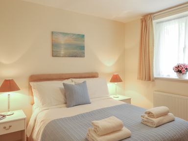 A bedroom with a bed, two bedside tables with lamps, folded towels on the bed, a painting on the wall, and a window with curtains and flowers at Willow Barn in Cucklington near Wincanton