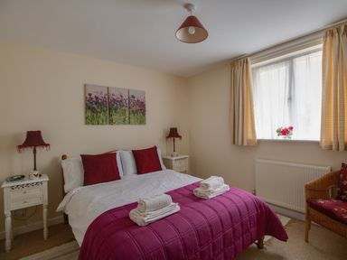 A bedroom with a double bed with red pillows and a purple quilt with towels on the bed at Little Barn in Cucklington near Wincanton