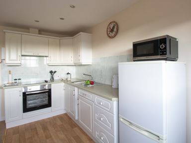 A kitchen with white cabinets a stove a sink fridge with microwave on top and a clock on the wall at Little Barn in Cucklington near Wincanton