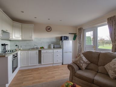 A kitchen with white cabinets a refrigerator and a beige sofa near a glass door at Little Barn in Cucklington near Wincanton