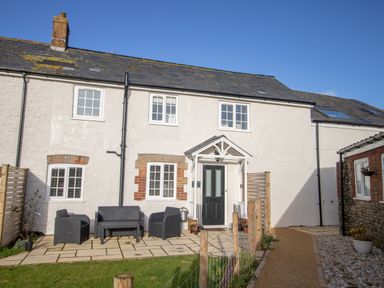 A front view of a white cottage with black door and outdoor seating on a paved path at Willowbrook Cottage in Litton Cheney
