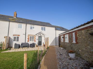 An outdoor patio area with garden chairs and a table next to a white cottage and a stone building at Willowbrook Cottage in Litton Cheney