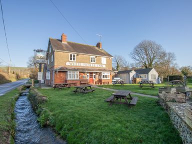 An outdoor area with picnic tables and a small stream next to a pub called White Horse Inn in a rural setting