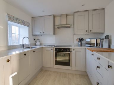 A kitchen with grey cabinets a sink an oven a microwave and a window at Willowbrook Cottage in Litton Cheney