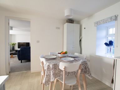 A dining area with a table set for four near a window and a cabinet with an ironing board nearby at Willowbrook Cottage in Litton Cheney
