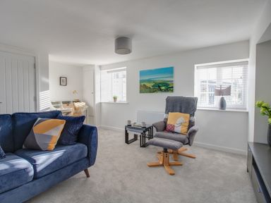 A living room with a blue sofa gray armchair small tables desk and windows at Willowbrook Cottage in Litton Cheney