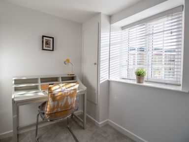 A small workspace with a desk chair with a cushion a plant on a windowsill and a small framed picture on the wall at Willowbrook Cottage in Litton Cheney