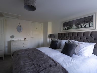 A bedroom with a bed with pillows and a blanket a dresser with a mirror and a lamp by the door at Willowbrook Cottage in Litton Cheney