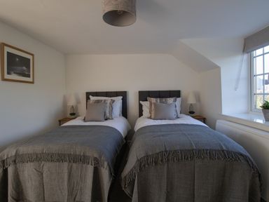 A bedroom with two single beds bedside tables lamps and a window at Willowbrook Cottage in Litton Cheney